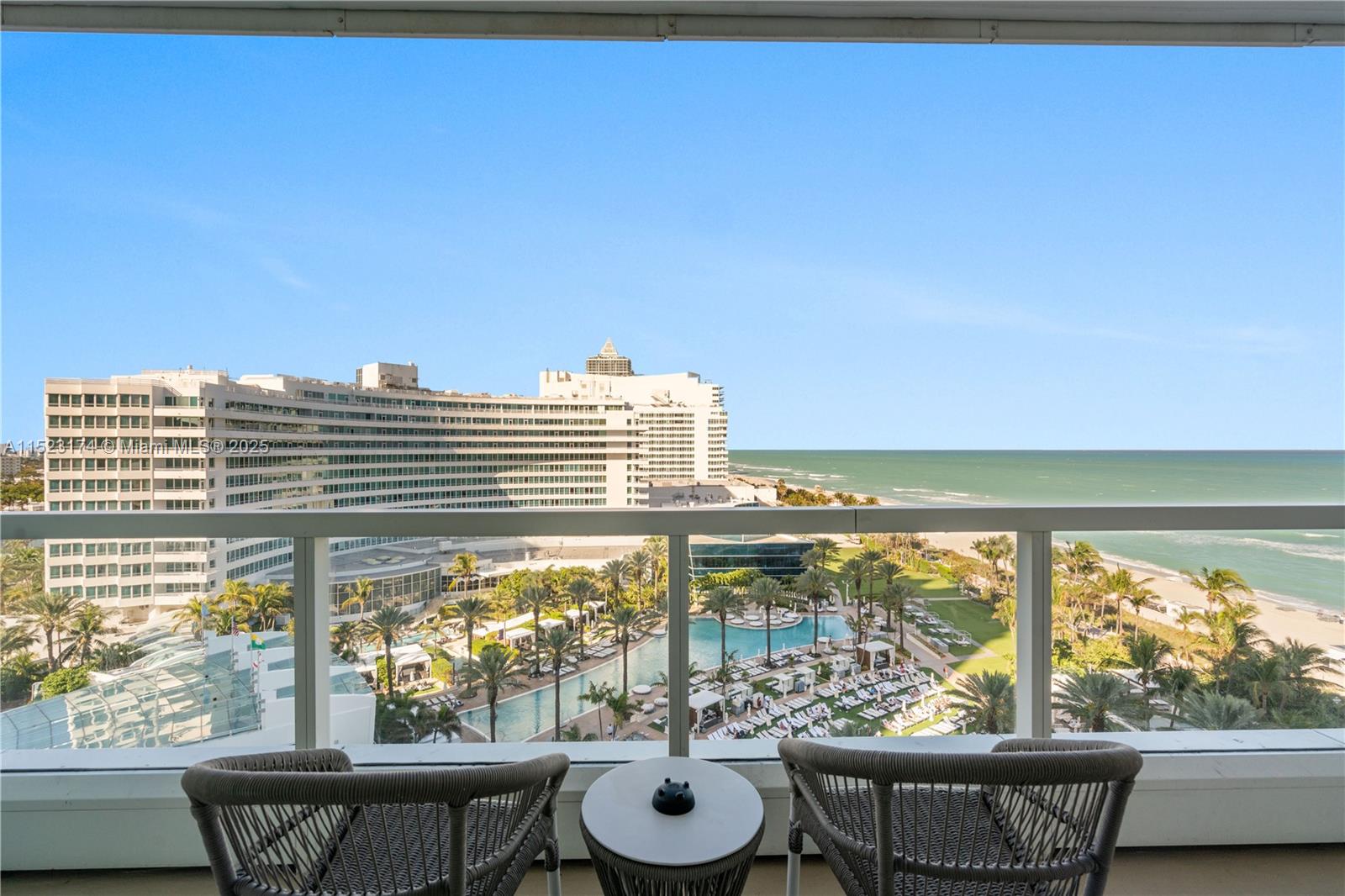 A balcony with two chairs and a table overlooks a resort pool and the ocean — 4391 COLLINS AV # 1007, Miami Beach FL 33140, MIAMI BEACH, FL