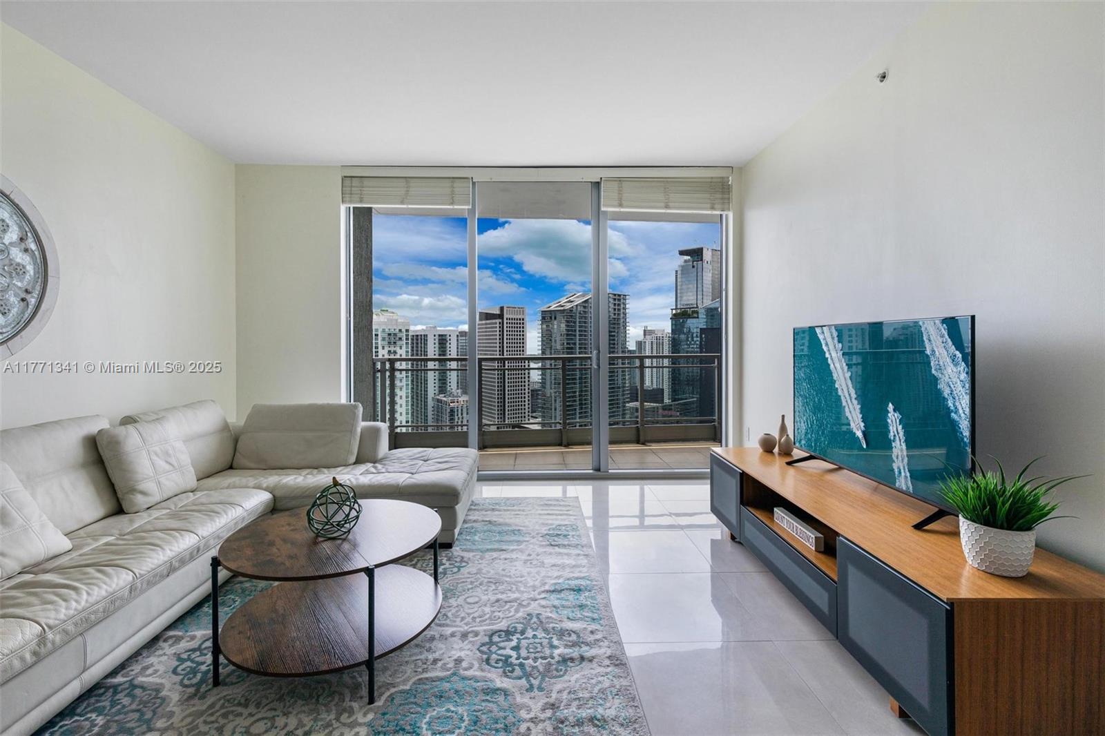 A modern living room features a white sectional sofa, a round coffee table, and city views — 90 SW 3rd St # 4103, Miami FL 33130, MIAMI, FL