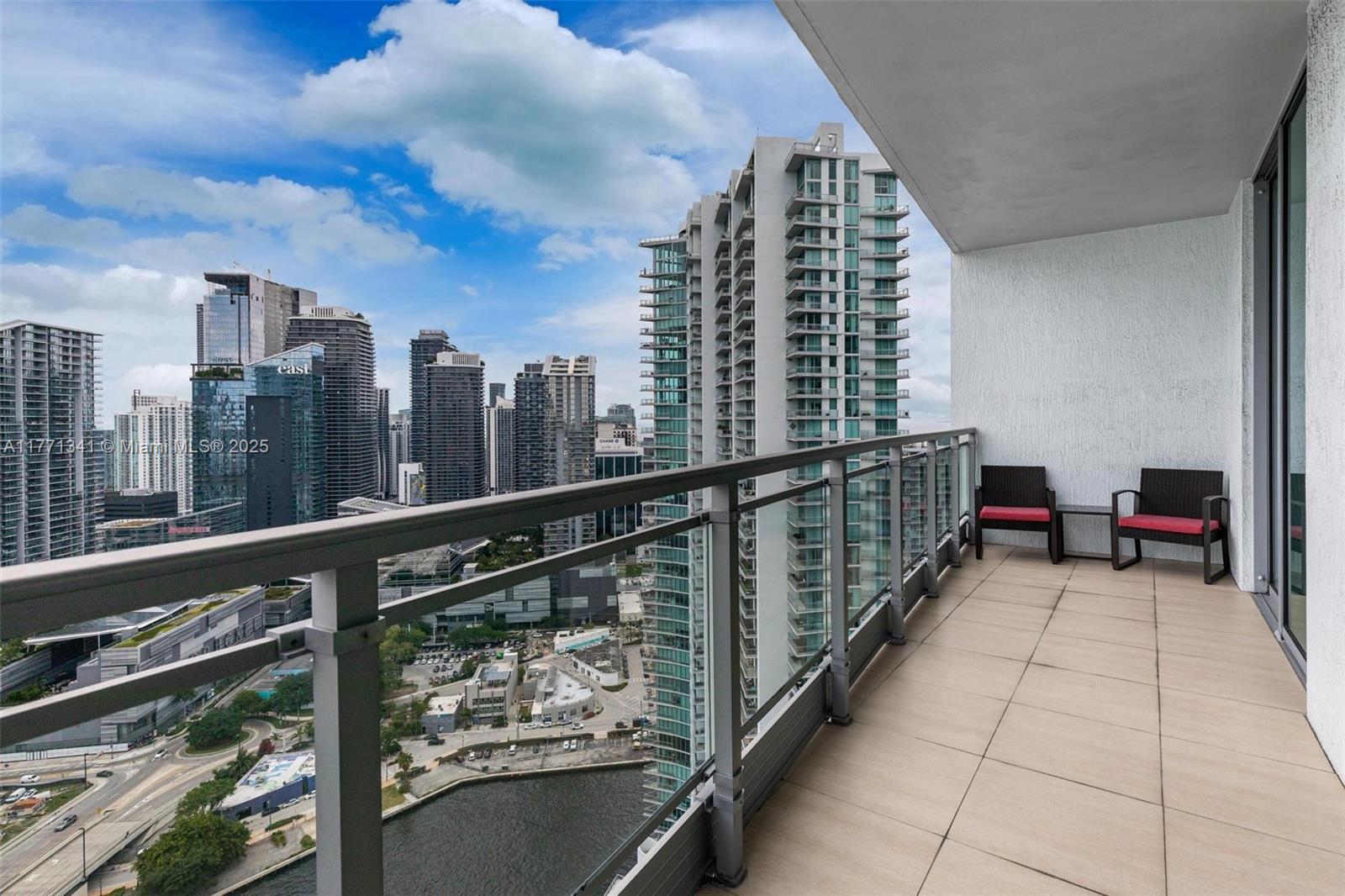 A balcony with tiled flooring and two chairs overlooks a dense urban skyline and water — 90 SW 3rd St # 4103, Miami FL 33130, MIAMI, FL