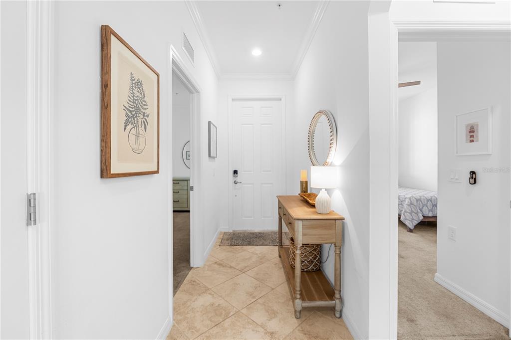 A bright entryway features tile flooring, a wooden console table, and doorways leading to bedrooms — 43000 GREENWAY BOULEVARD UNIT 145, PUNTA GORDA, FL
