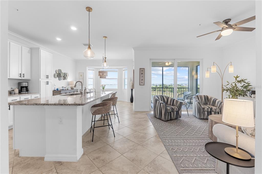 An open-concept kitchen and living area features white cabinetry, granite countertops, and a sliding glass door — 43000 GREENWAY BOULEVARD UNIT 145, PUNTA GORDA, FL