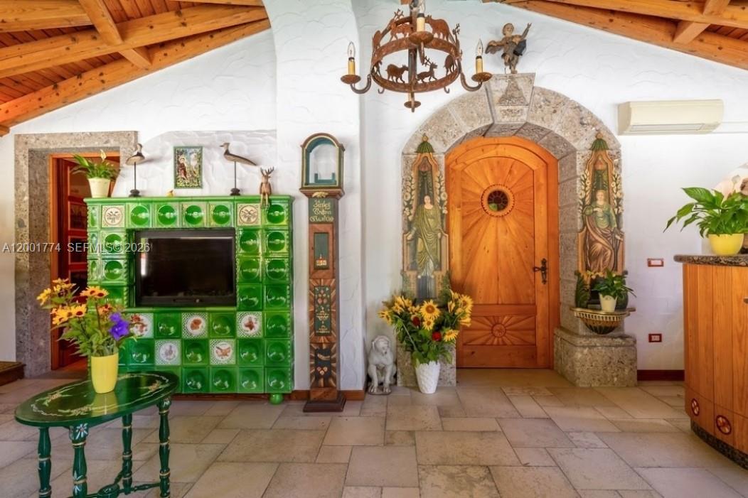 A room features a green tiled fireplace, a wooden arched door, and a rustic chandelier — 5 Via Giuseppe Verdi, Fusine in Valromana, Tarvisio, FL