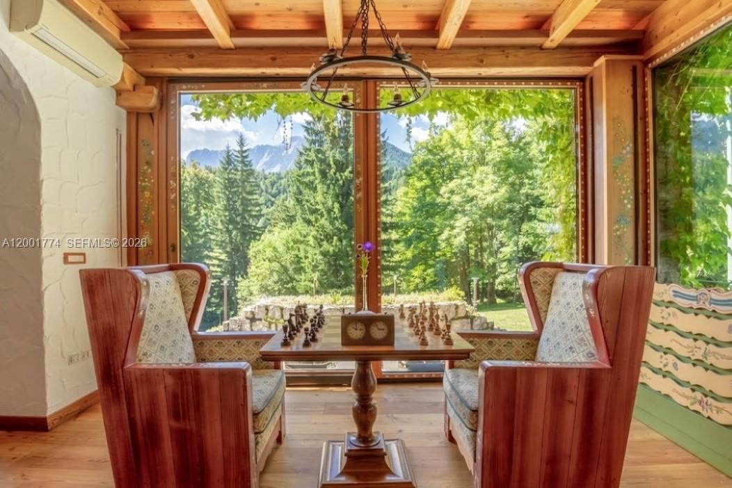 A sunroom features a wooden chess table between two armchairs facing a large mountain view — 5 Via Giuseppe Verdi, Fusine in Valromana, Tarvisio, FL