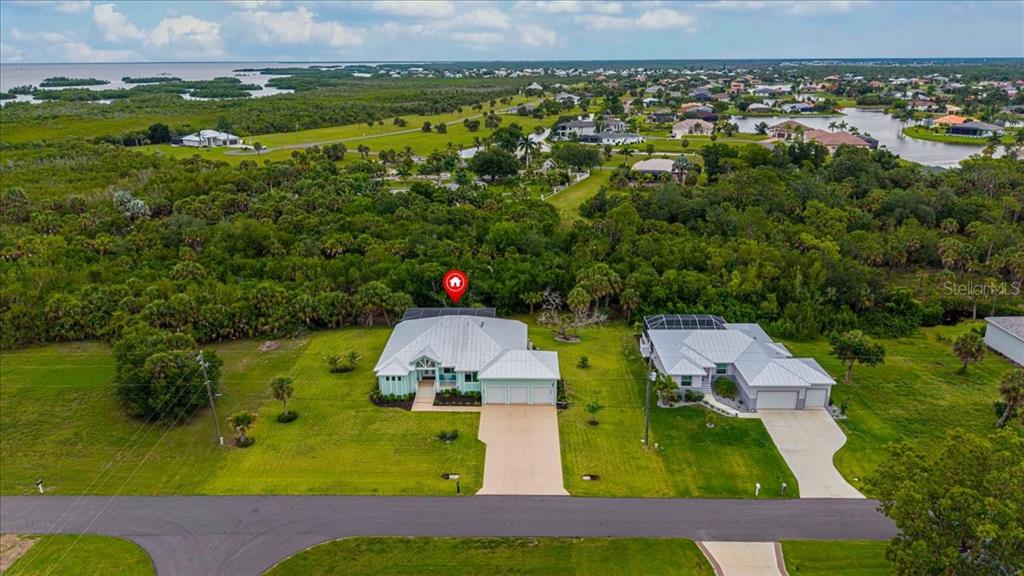 An aerial view shows two suburban houses with metal roofs surrounded by dense green vegetation — 16883 ACAPULCO ROAD, PUNTA GORDA, FL