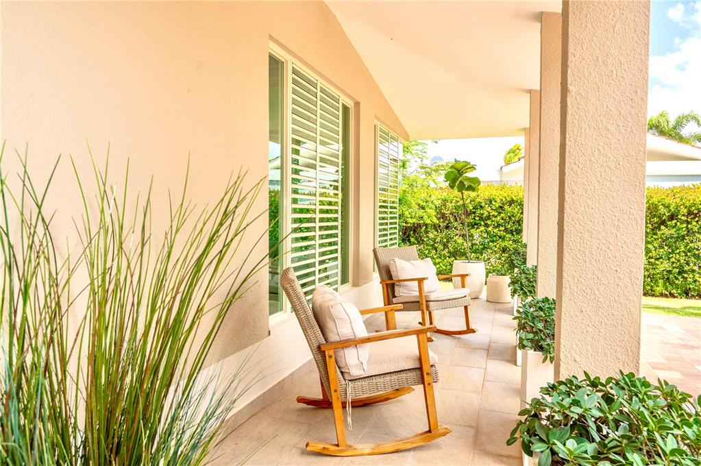 A covered patio features two wooden rocking chairs, potted plants, and light-colored tile flooring — 302 CAMINO DE LOS CEDROS, DORADO, PR