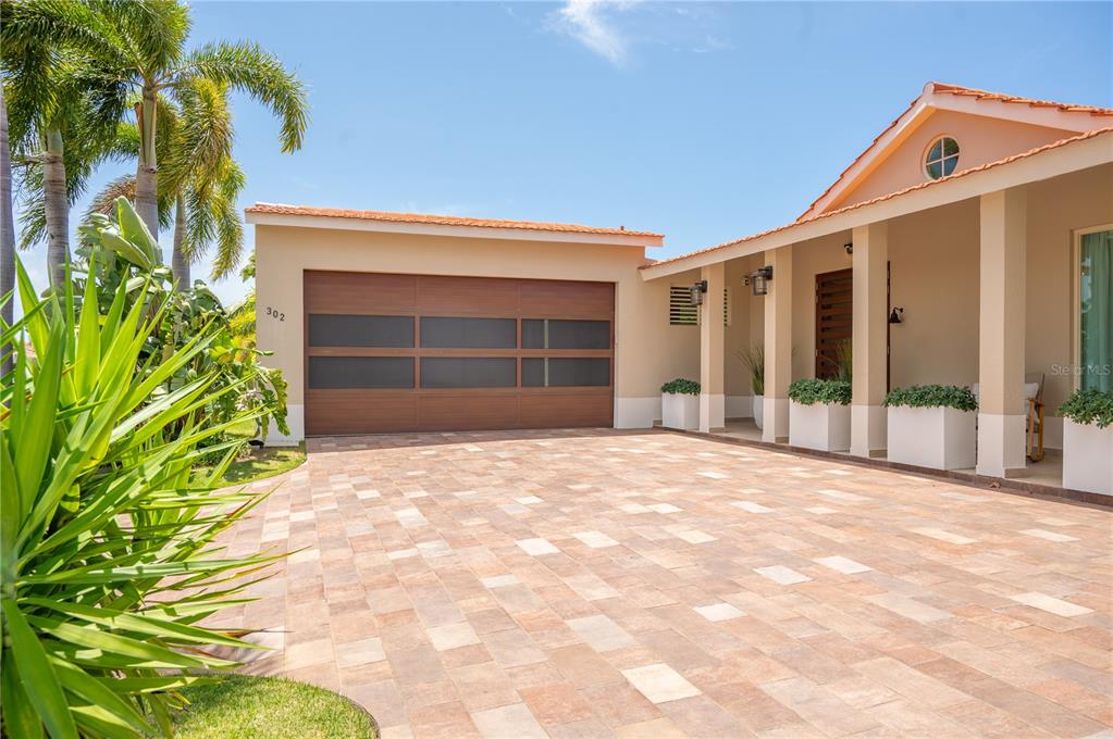 A modern house exterior features a wood-paneled garage door, a paved driveway, and palm trees — 302 CAMINO DE LOS CEDROS, DORADO, PR