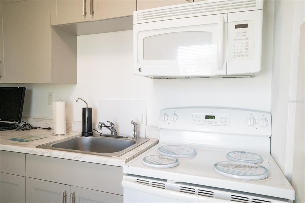 A kitchen features a white stove, a microwave, a sink, and light-colored cabinetry — 3227 5TH AVE S, ST PETERSBURG, FL