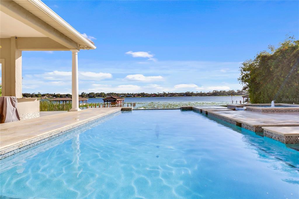 A swimming pool with a spa overlooks a lake from a covered patio — 9245 SOUTHERN BREEZE DRIVE, ORLANDO, FL