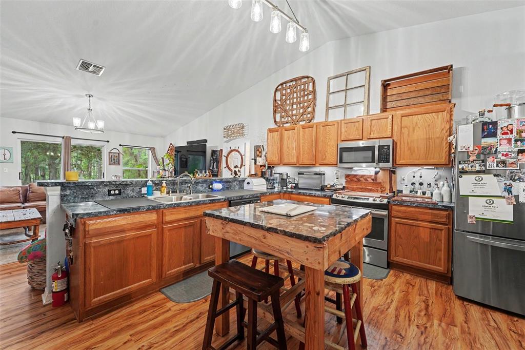 A kitchen features wood cabinets, a granite-topped island, and stainless steel appliances under vaulted ceilings — 1210 W FAN DRIVE, CITRUS SPRINGS, FL