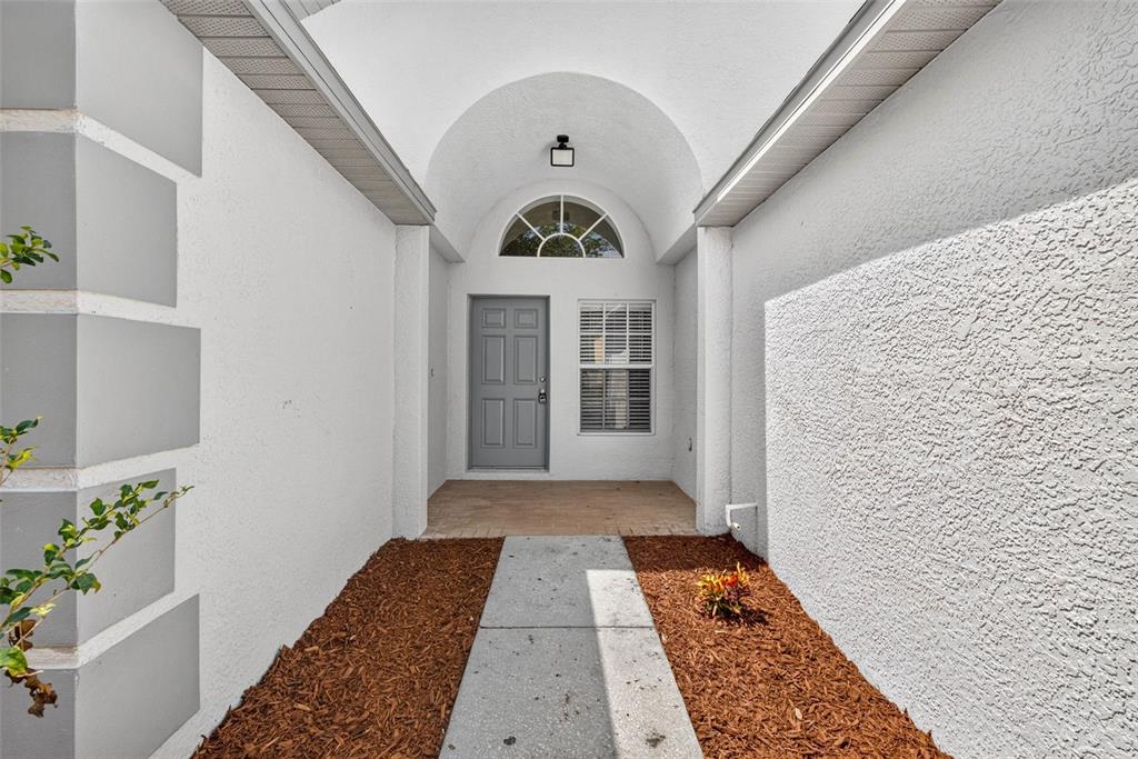 A gray front door sits beneath a vaulted entryway with a semi-circular window above — 25442 BRUFORD BOULEVARD, LAND O LAKES, FL