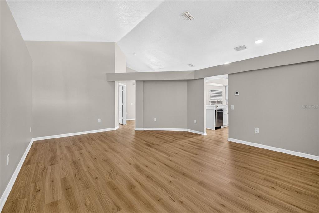 An empty living room features light gray walls, vaulted ceilings, and wood-look vinyl plank flooring — 25442 BRUFORD BOULEVARD, LAND O LAKES, FL