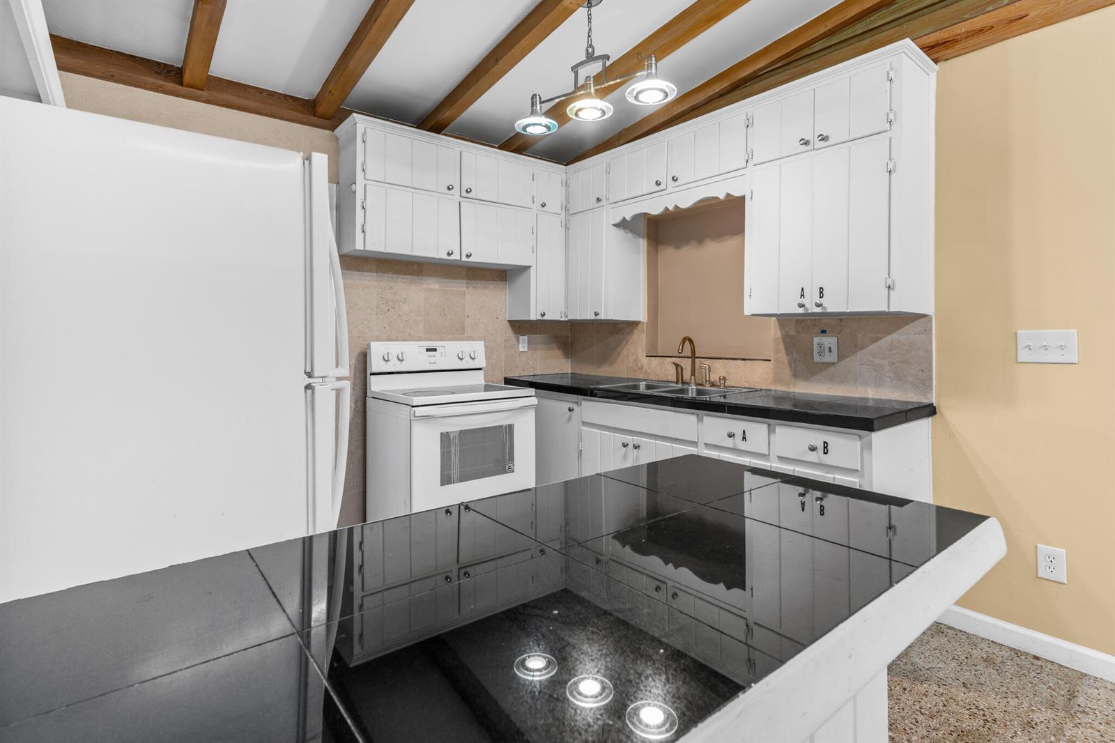 A kitchen features white cabinets, black countertops, a white stove, and exposed wooden ceiling beams — 2456 Cortez Avenue, Vero Beach FL 32960, VERO BEACH, FL