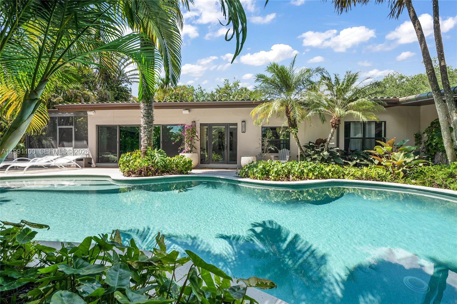 A swimming pool sits in front of a single-story house with palm trees and landscaping — 3620 Battersea Rd, Miami FL 33133, MIAMI, FL