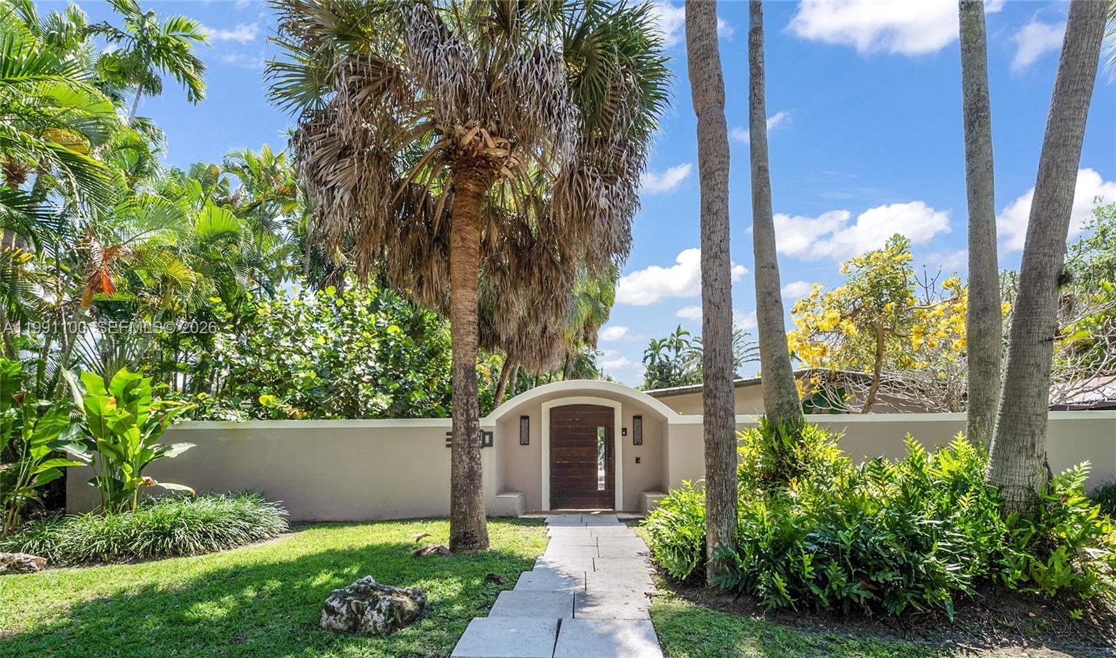A stone path leads to a wooden arched door set in a beige privacy wall — 3620 Battersea Rd, Miami FL 33133, MIAMI, FL