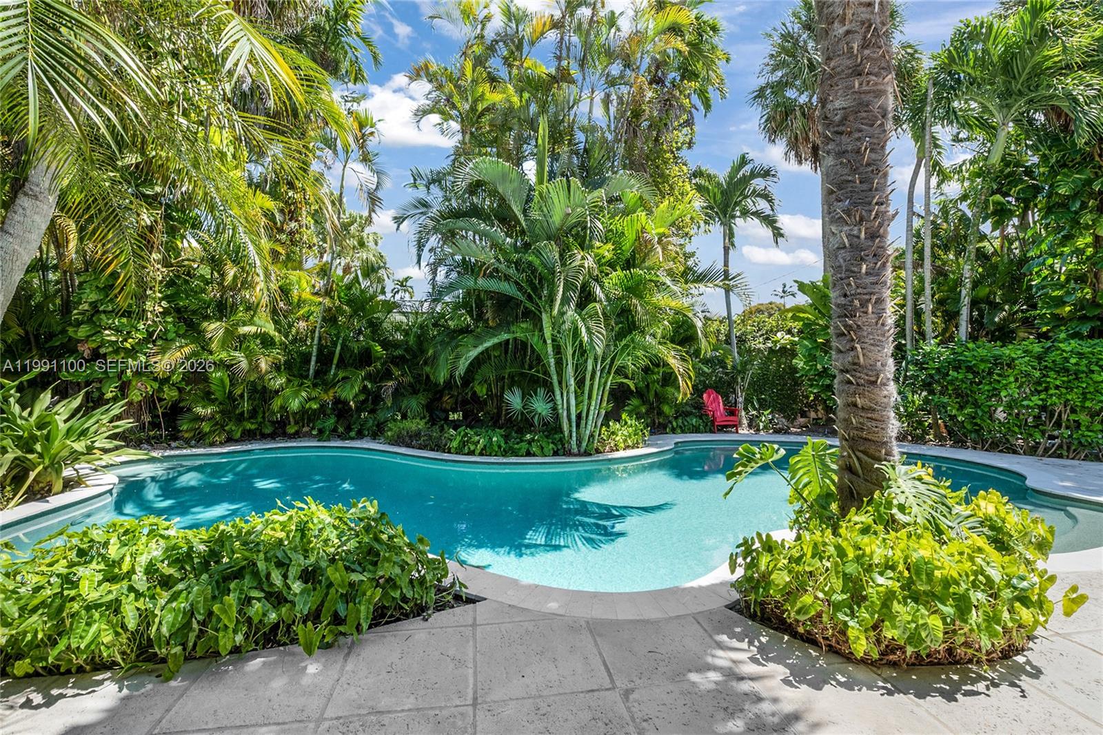 A curved swimming pool is surrounded by lush tropical landscaping and a stone patio — 3620 Battersea Rd, Miami FL 33133, MIAMI, FL