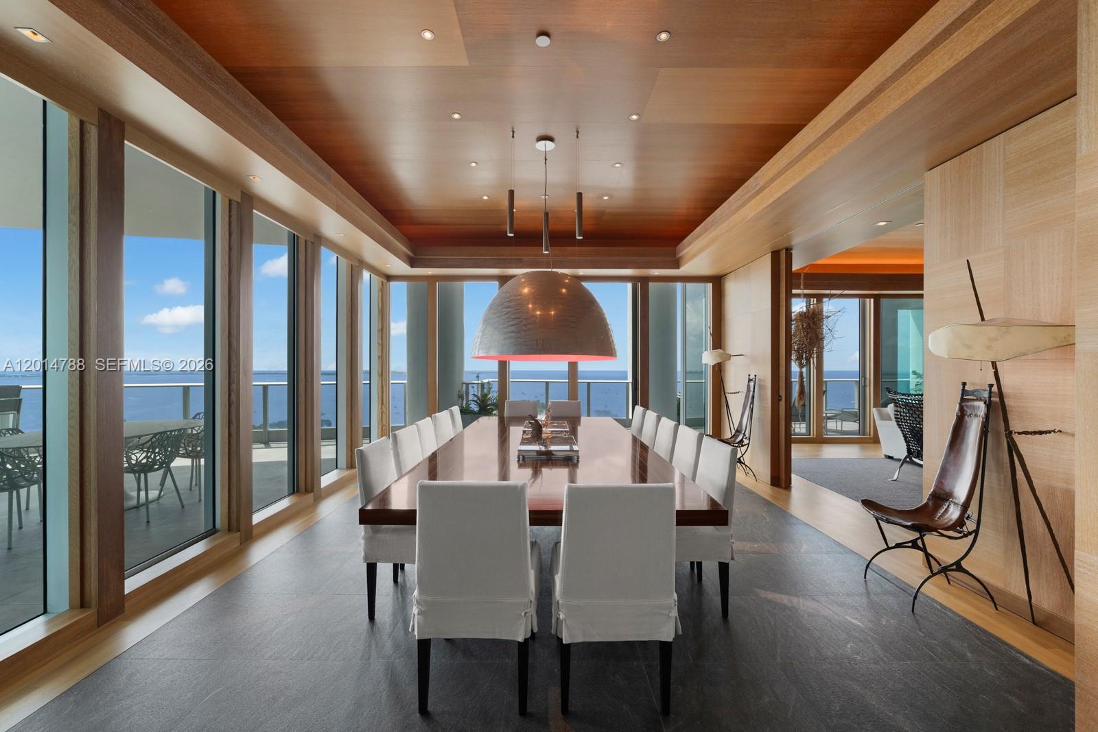 A dining room features a long wooden table, white chairs, and floor-to-ceiling ocean views — 2627 S Bayshore Dr # 3201, Miami FL 33133, MIAMI, FL
