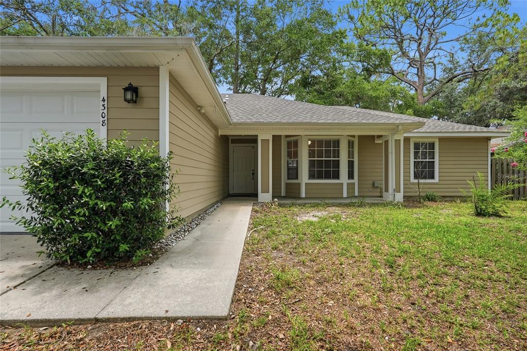 A tan, single-story house features a concrete walkway leading to a recessed front entrance — 4308 NW 35TH TERRACE, GAINESVILLE, FL