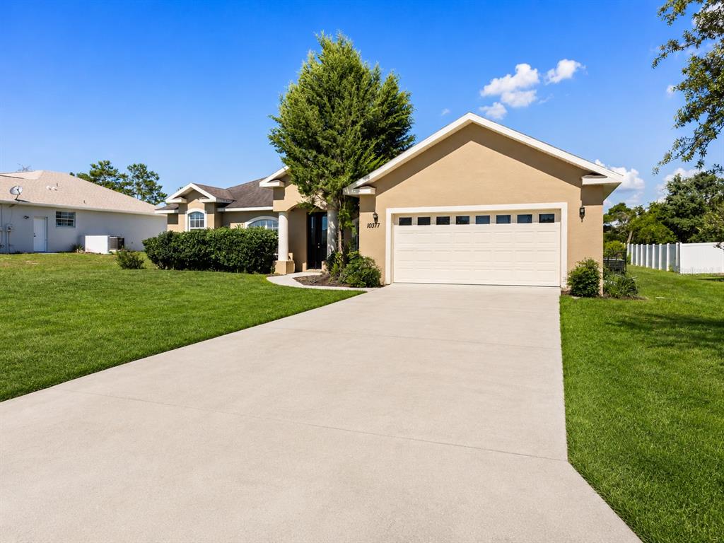 A single-story suburban house with a tan stucco exterior, two-car garage, and concrete driveway — 10377 SW 38TH AVENUE, OCALA, FL