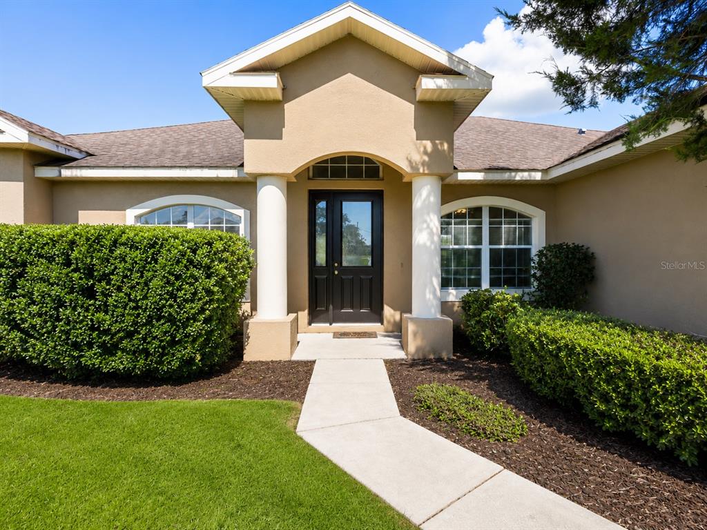 The exterior of a house features a tan facade, white columns, and a dark front door — 10377 SW 38TH AVENUE, OCALA, FL