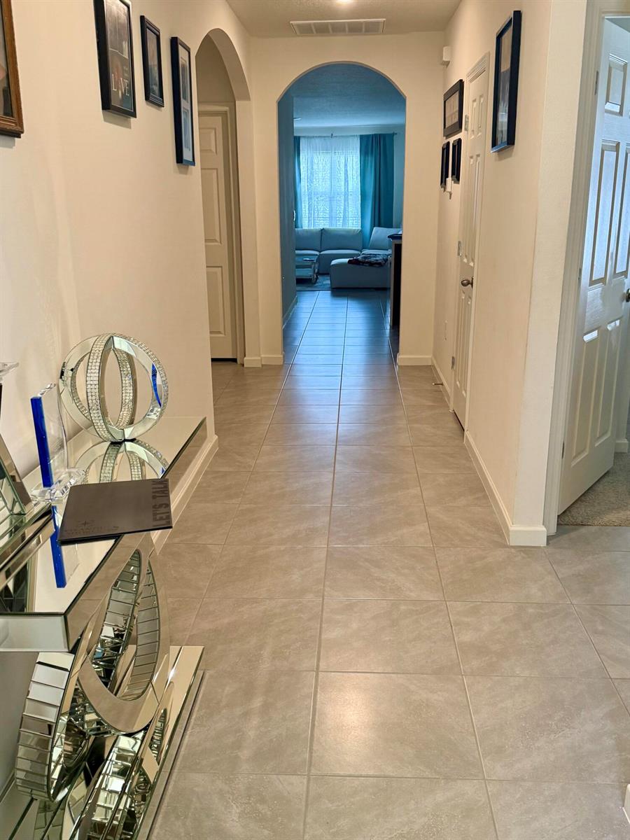 A tiled hallway leads through an arched doorway toward a living room with blue curtains — 1405 Pace Drive NW, Palm Bay FL 32907, PALM BAY, FL
