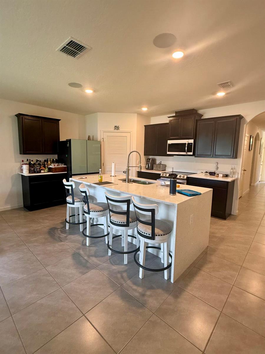 A kitchen features dark cabinetry, a large central island with bar seating, and tile flooring — 1405 Pace Drive NW, Palm Bay FL 32907, PALM BAY, FL