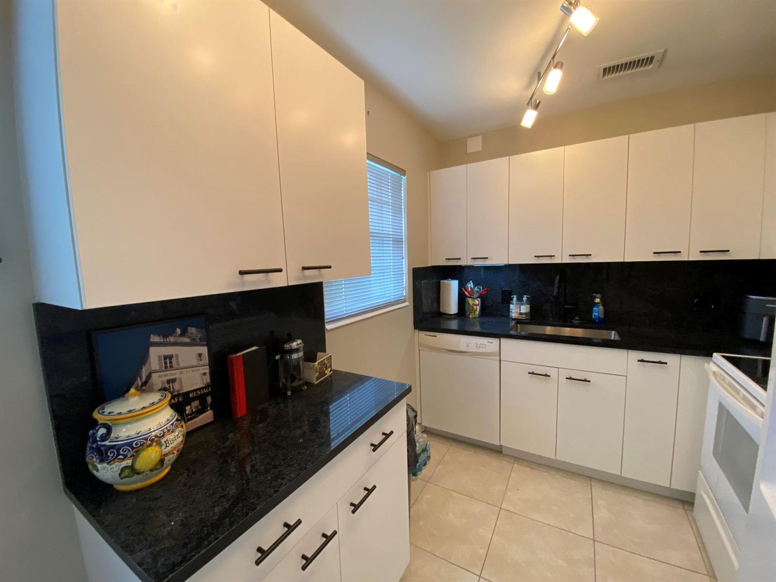 A kitchen features white cabinets, black countertops, a stainless steel sink, and tile flooring — 80 Prescott D # 80, Deerfield Beach FL 33442, DEERFIELD BEACH, FL