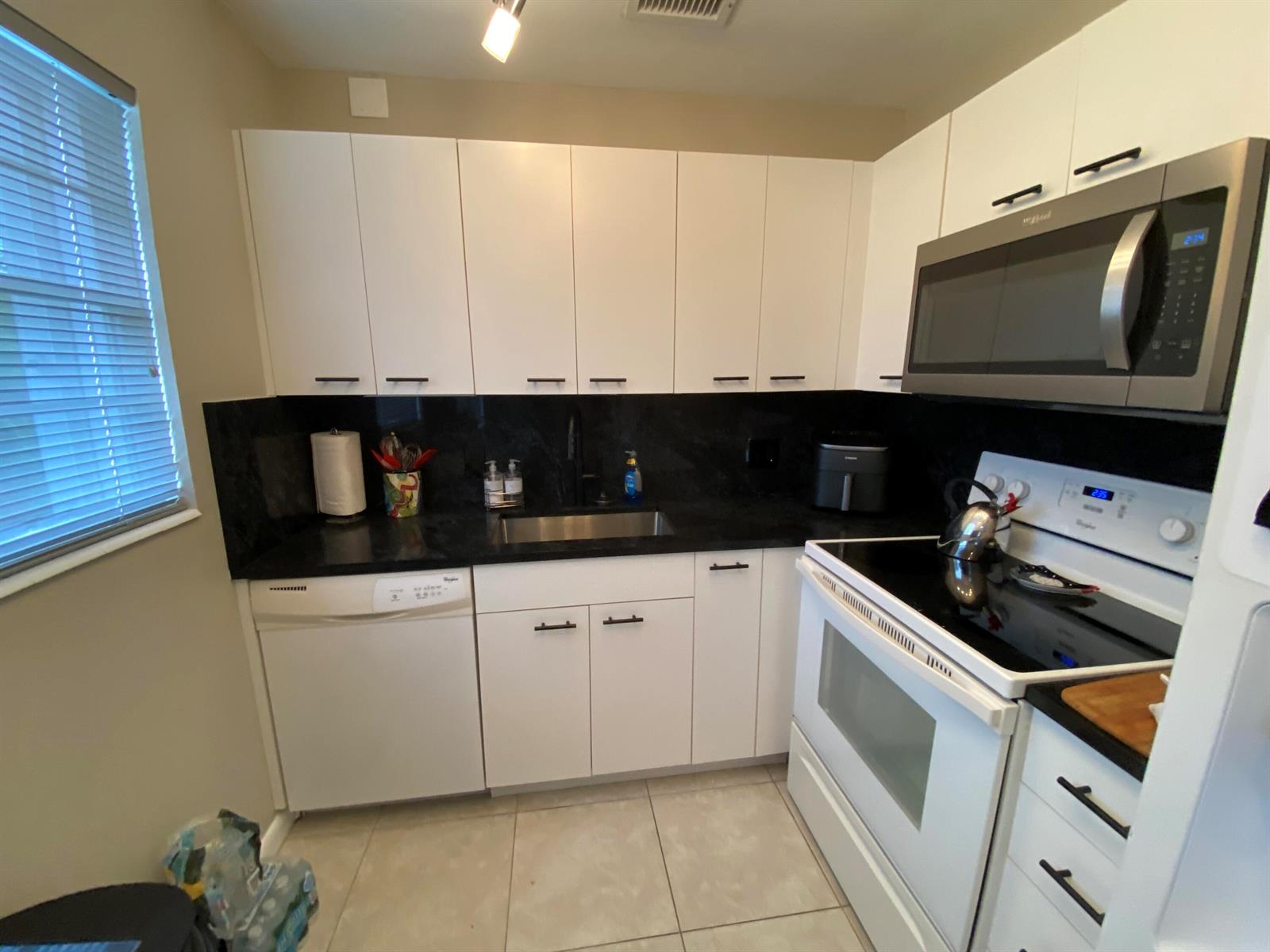 A kitchen features white cabinets, black countertops, a stainless steel sink, and white appliances — 80 Prescott D # 80, Deerfield Beach FL 33442, DEERFIELD BEACH, FL