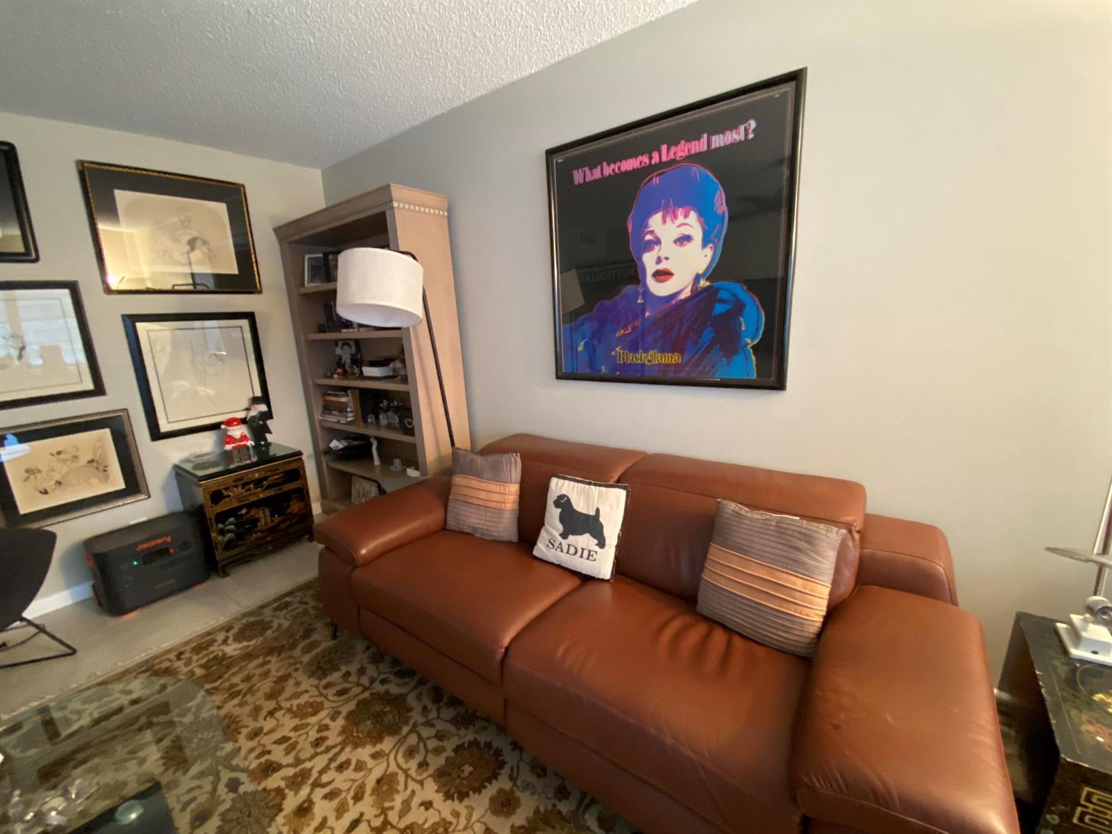 A living room features a brown leather sofa, a large framed poster, and a bookshelf — 80 Prescott D # 80, Deerfield Beach FL 33442, DEERFIELD BEACH, FL