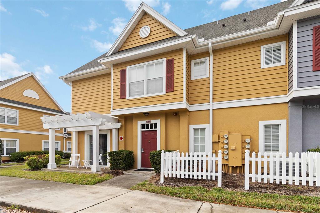 A two-story yellow townhouse with a white pergola, a red front door, and white fencing — 2620 LODI CIRCLE UNIT 101, KISSIMMEE, FL