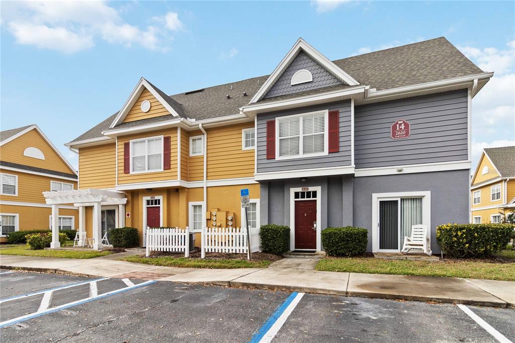 A two-story apartment building with yellow and gray siding, a white fence, and parking spaces — 2620 LODI CIRCLE UNIT 101, KISSIMMEE, FL