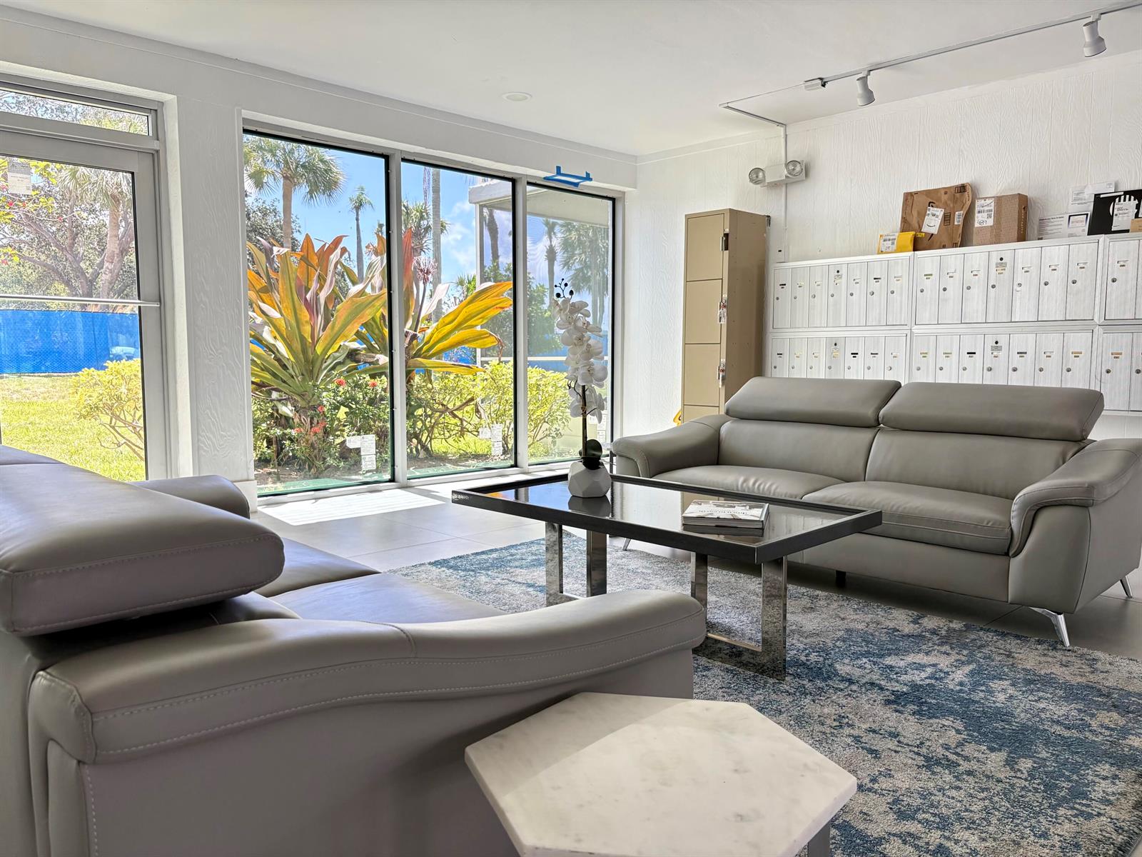 A bright lounge area features two grey leather sofas, a glass coffee table, and mailboxes — 5700 NW 2nd Avenue # 203, Boca Raton FL 33487, BOCA RATON, FL
