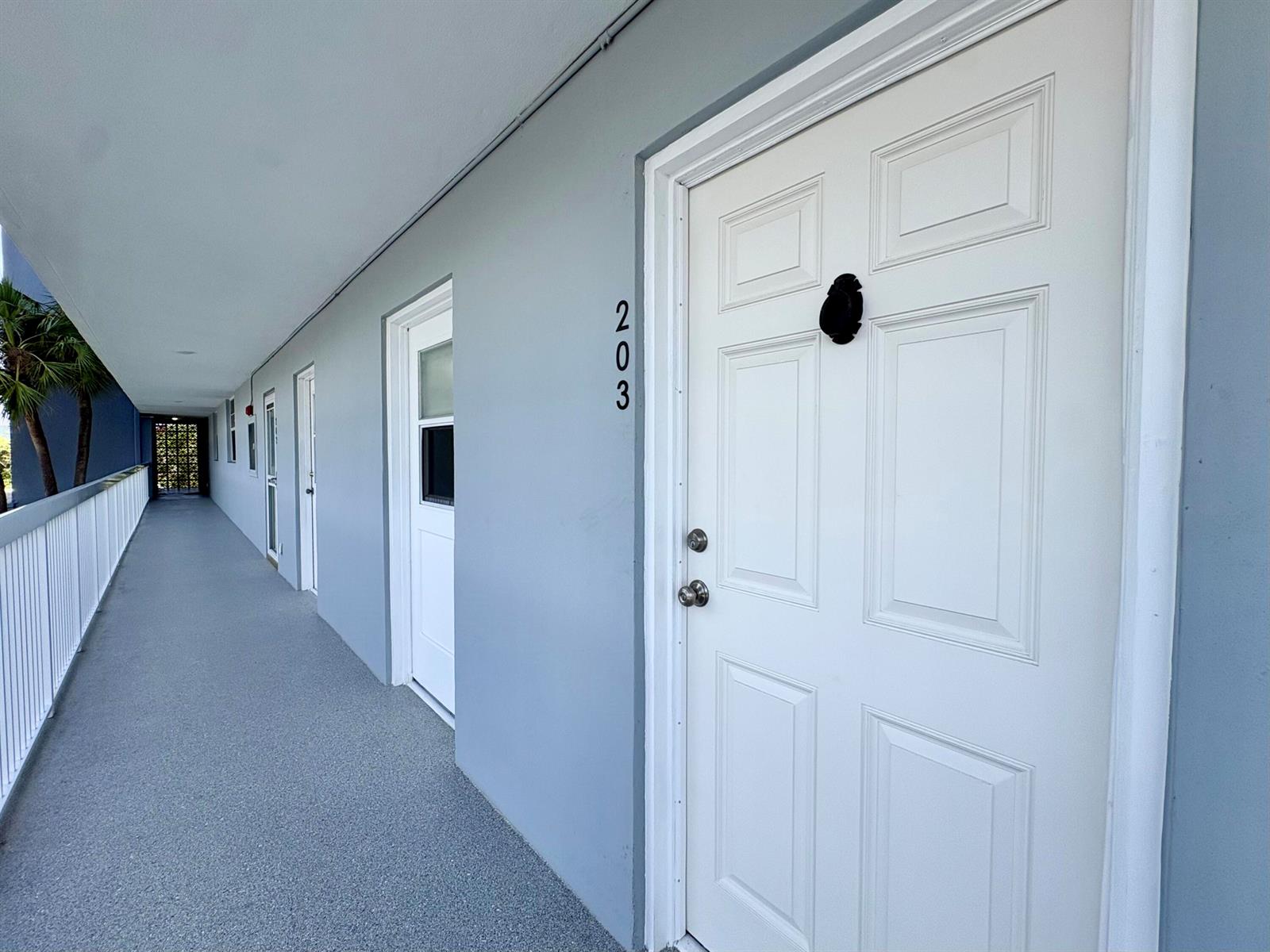 An exterior hallway with white doors, numbered 203, and a metal railing along the side — 5700 NW 2nd Avenue # 203, Boca Raton FL 33487, BOCA RATON, FL