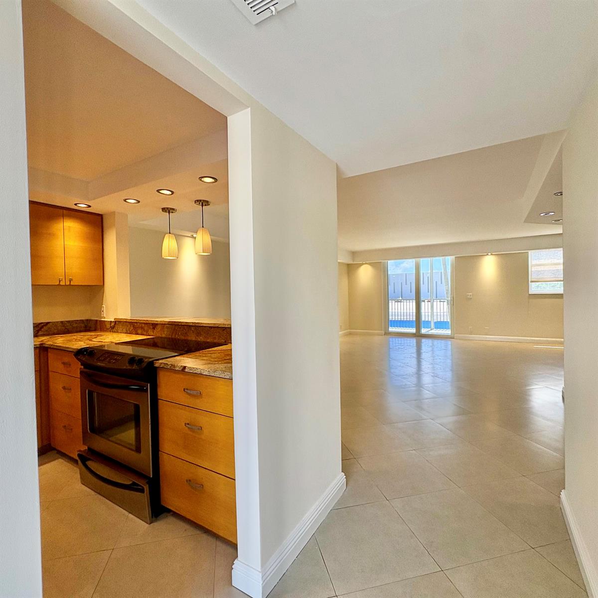 A kitchen with wood cabinets and granite countertops opens into a spacious, tiled living area — 5700 NW 2nd Avenue # 203, Boca Raton FL 33487, BOCA RATON, FL