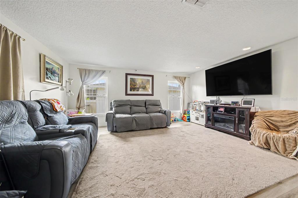 A living room features gray sofas, a large wall-mounted television, and beige carpeting — 394 BARBERRY LANE, ALTAMONTE SPRINGS, FL