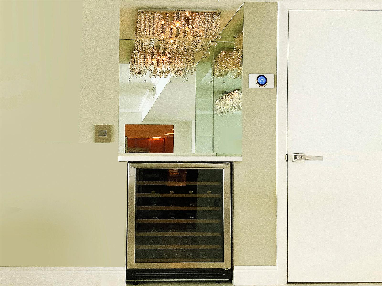 A wine cooler sits beneath a mirror and crystal chandelier next to a white door — 3460 S Ocean Boulevard # 7110, Palm Beach FL 33480, PALM BEACH, FL