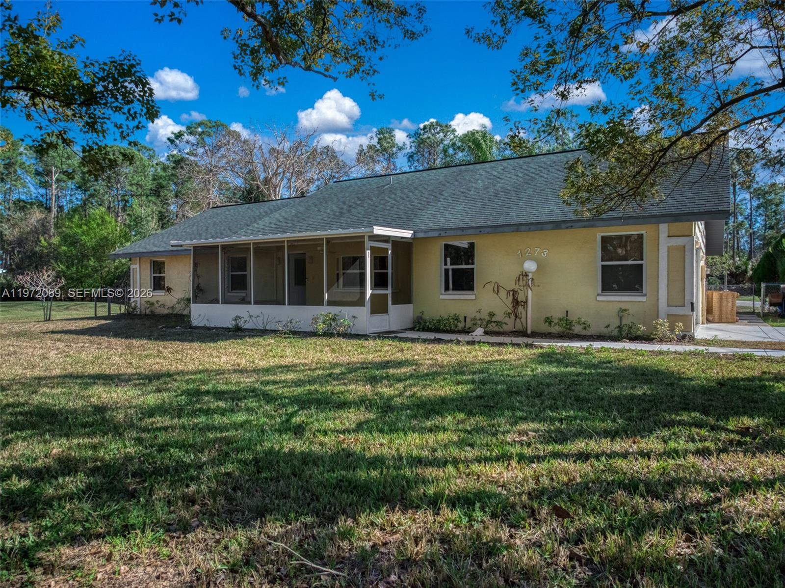 A yellow single-story house features a screened-in front porch and a dark shingled roof — 1273 Woodbury Avenue, Sebring FL 33875, SEBRING, FL