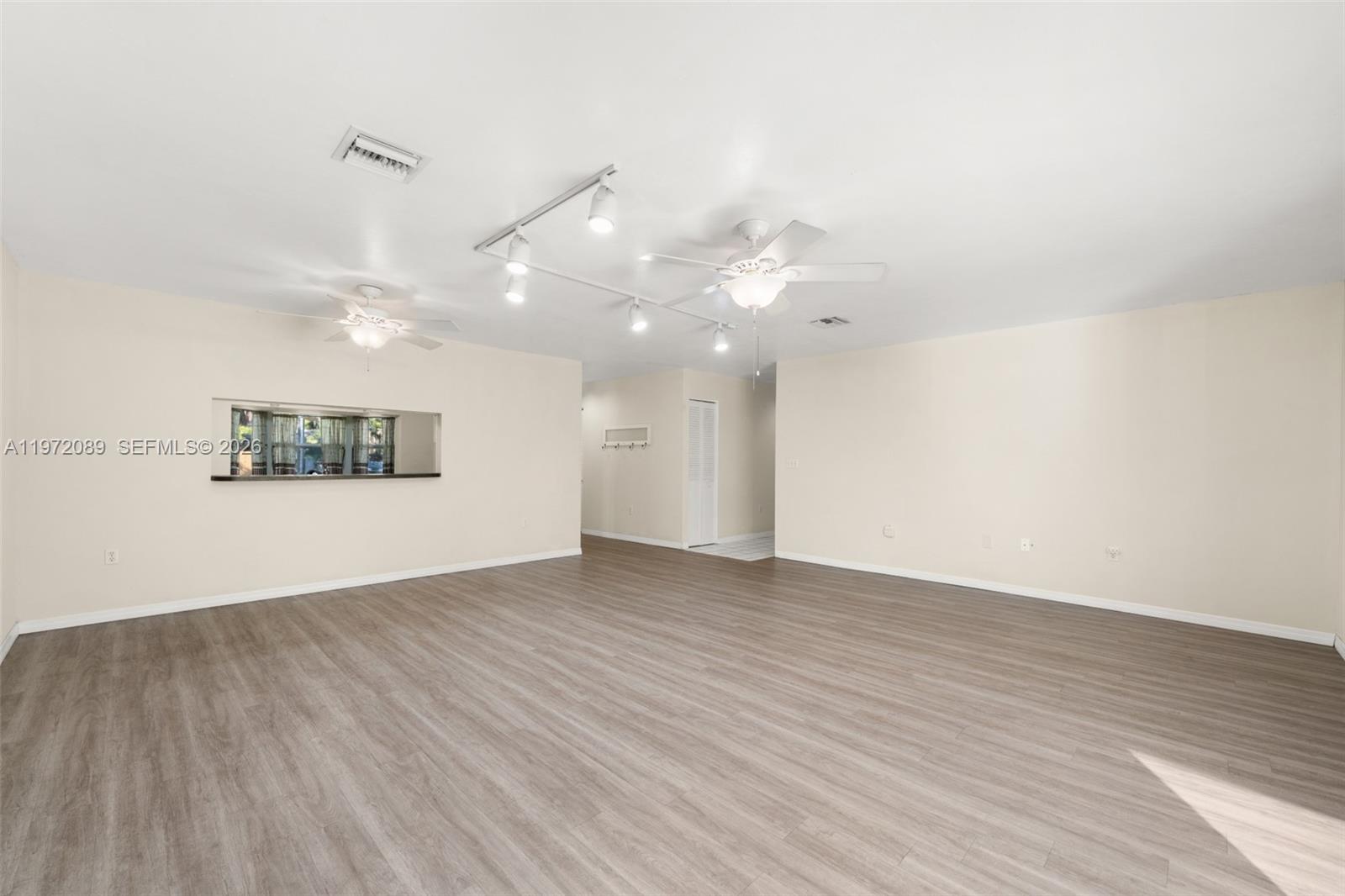 A spacious, empty living room features light wood-look flooring, track lighting, and two ceiling fans — 1273 Woodbury Avenue, Sebring FL 33875, SEBRING, FL