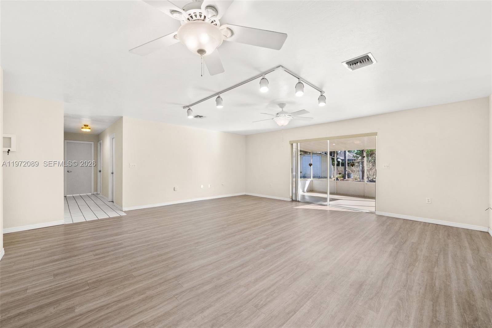 A spacious living room features light wood-look flooring, a ceiling fan, and track lighting — 1273 Woodbury Avenue, Sebring FL 33875, SEBRING, FL