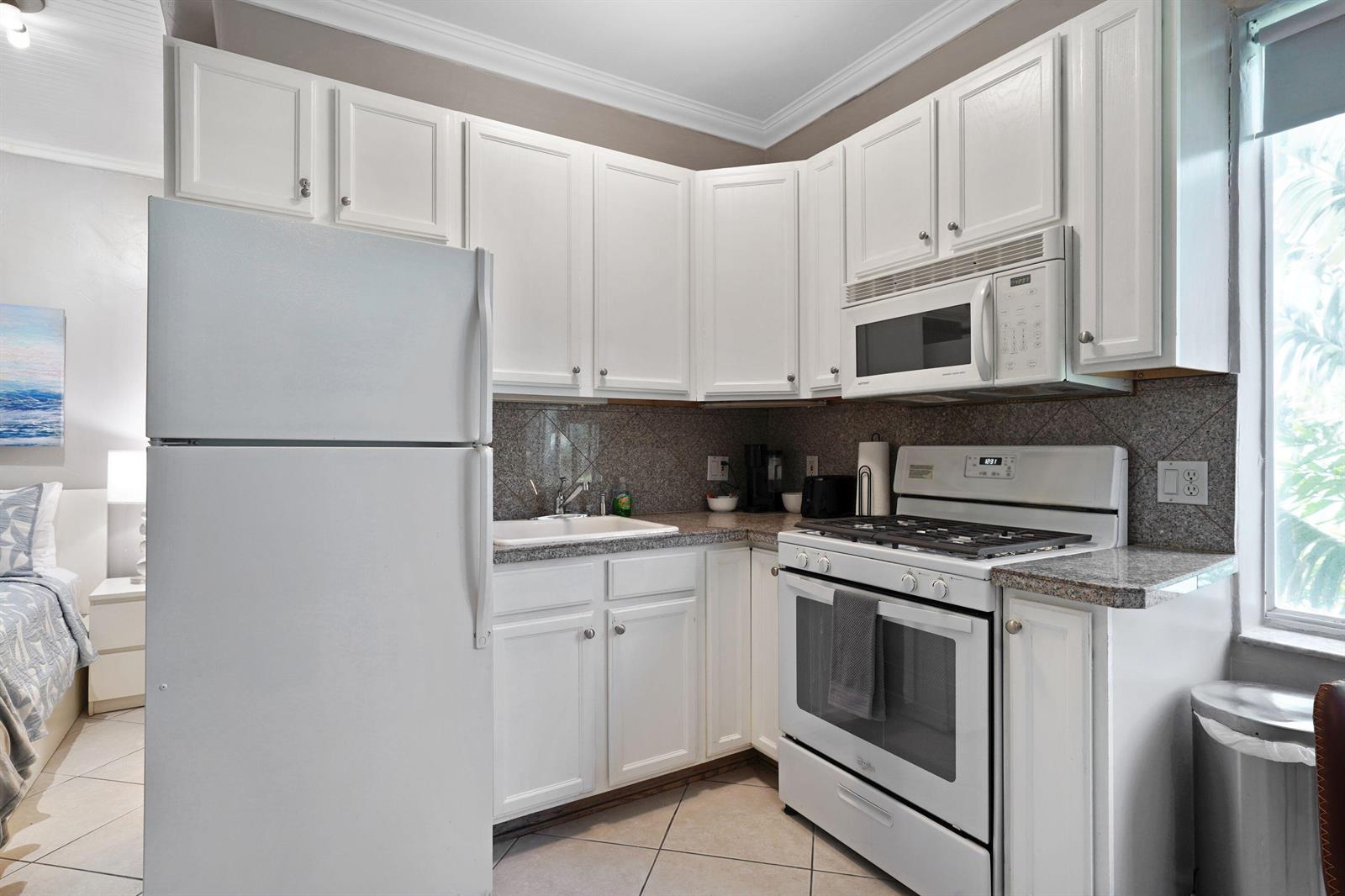 A small kitchen features white cabinets, white appliances, and granite countertops — 3710 Collins Avenue # 304, Miami Beach FL 33140, MIAMI BEACH, FL