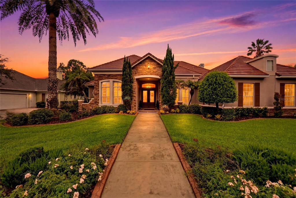A single-story house with a stone facade, tile roof, and a palm tree at sunset — 1059 CEASARS COURT, MOUNT DORA, FL