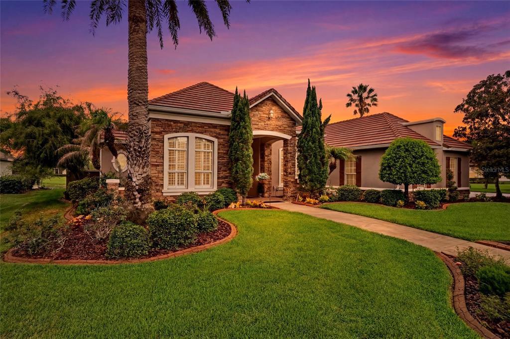 A stone-faced house with a tiled roof and landscaped lawn under a sunset sky — 1059 CEASARS COURT, MOUNT DORA, FL