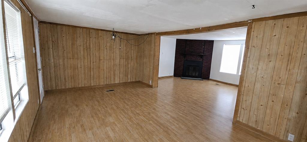 A living room features wood-paneled walls, light wood-look flooring, and a dark brick fireplace — 702 DAVID AVENUE, INTERLACHEN, FL