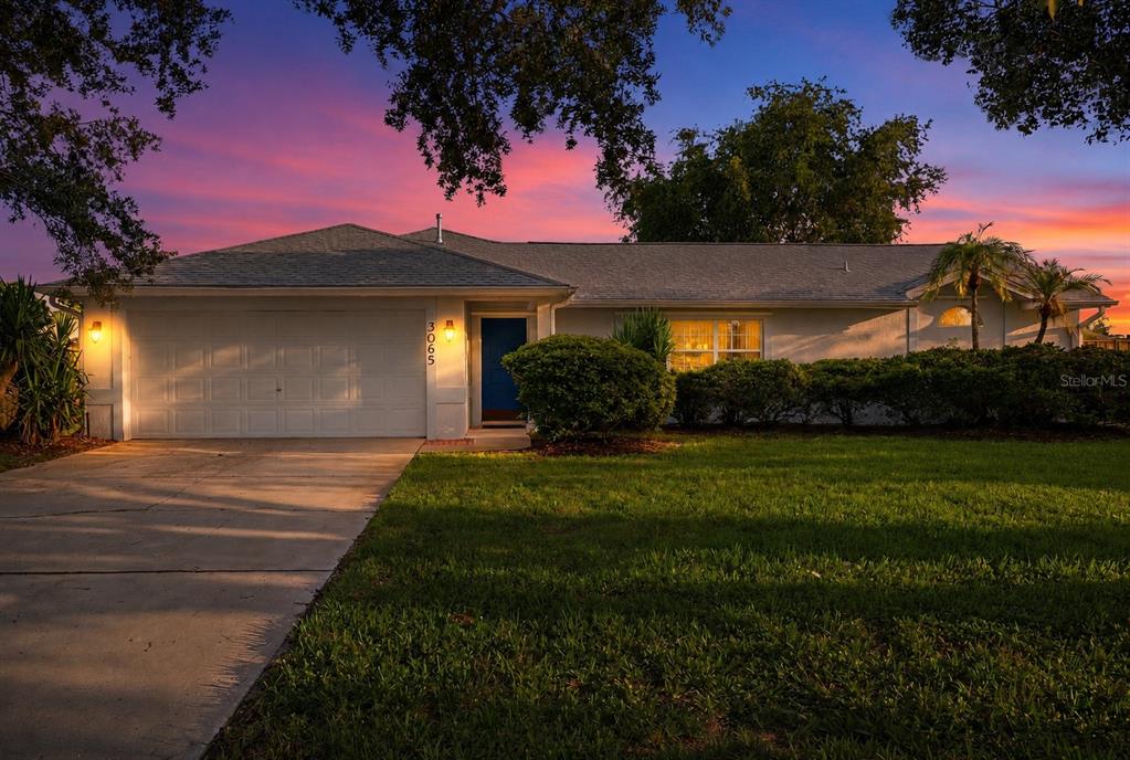 A single-story house with a white garage and a blue front door at sunset — 3065 PINEDA CROSSING DRIVE, MELBOURNE, FL