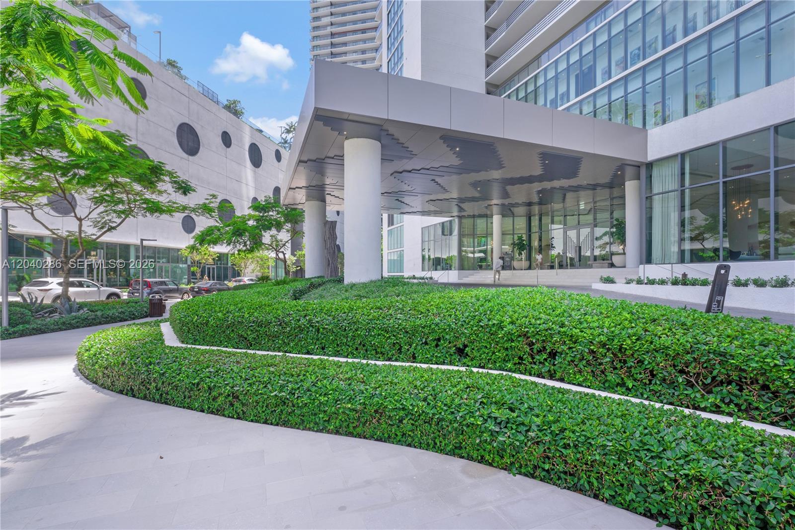A modern building entrance features a large canopy, white columns, and tiered green hedges — 650 NE 32nd St # 703, Miami FL 33137, MIAMI, FL