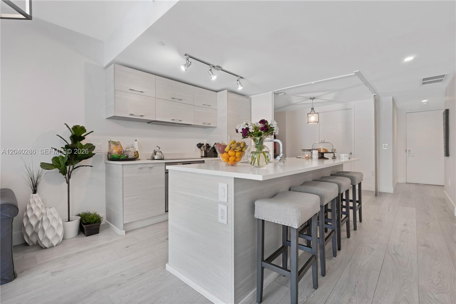 A modern kitchen features light wood cabinetry, a white quartz island, and four gray barstools — 650 NE 32nd St # 703, Miami FL 33137, MIAMI, FL