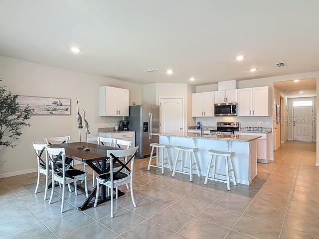 A kitchen and dining area feature white cabinetry, stainless steel appliances, and tile flooring — 2219 LAKE PRESERVE CIRCLE, NEW SMYRNA BEACH, FL