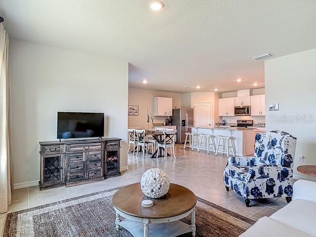 An open-concept living room features a television console, a coffee table, and a floral armchair — 2219 LAKE PRESERVE CIRCLE, NEW SMYRNA BEACH, FL