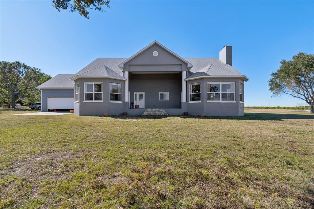 The rear exterior of a gray house features a covered patio and a detached garage — 2307 CASS ROAD, LAKE ALFRED, FL