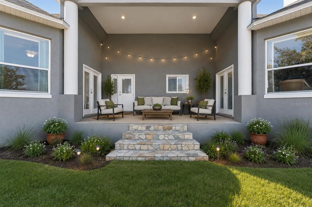 A covered patio features stone steps, outdoor furniture, and string lights against a gray exterior — 2307 CASS ROAD, LAKE ALFRED, FL