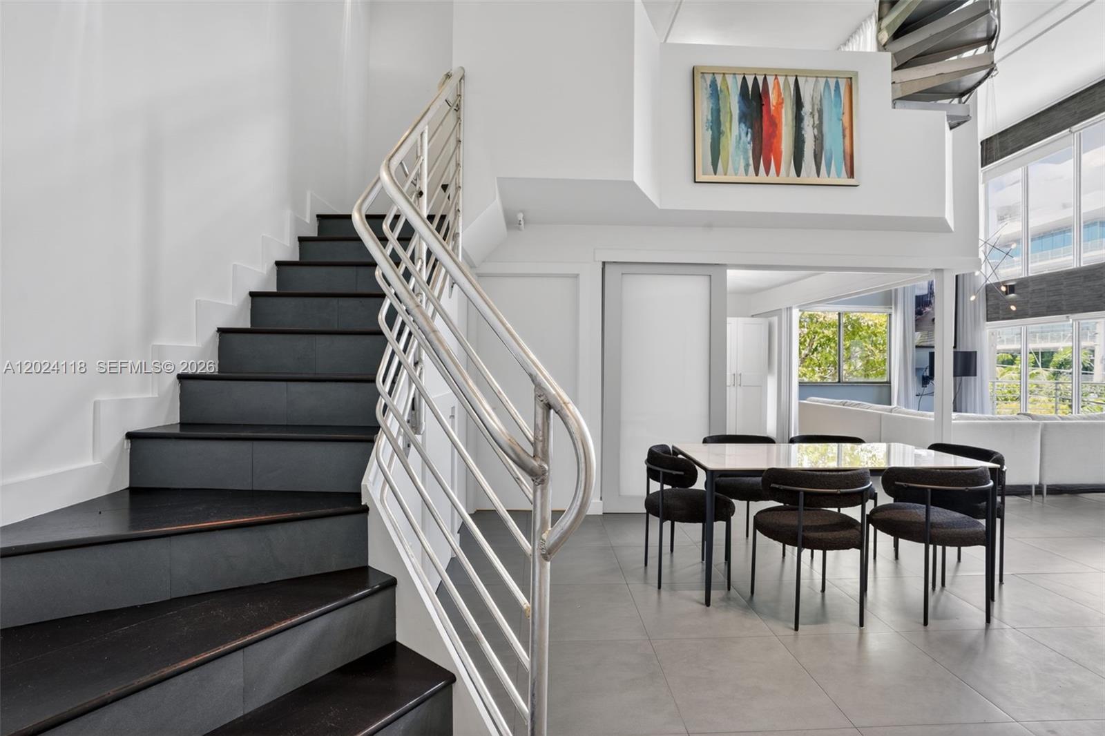 A modern interior features a dark staircase with metal railings next to a dining area — 900 4th St # 6, Miami Beach FL 33139, MIAMI BEACH, FL